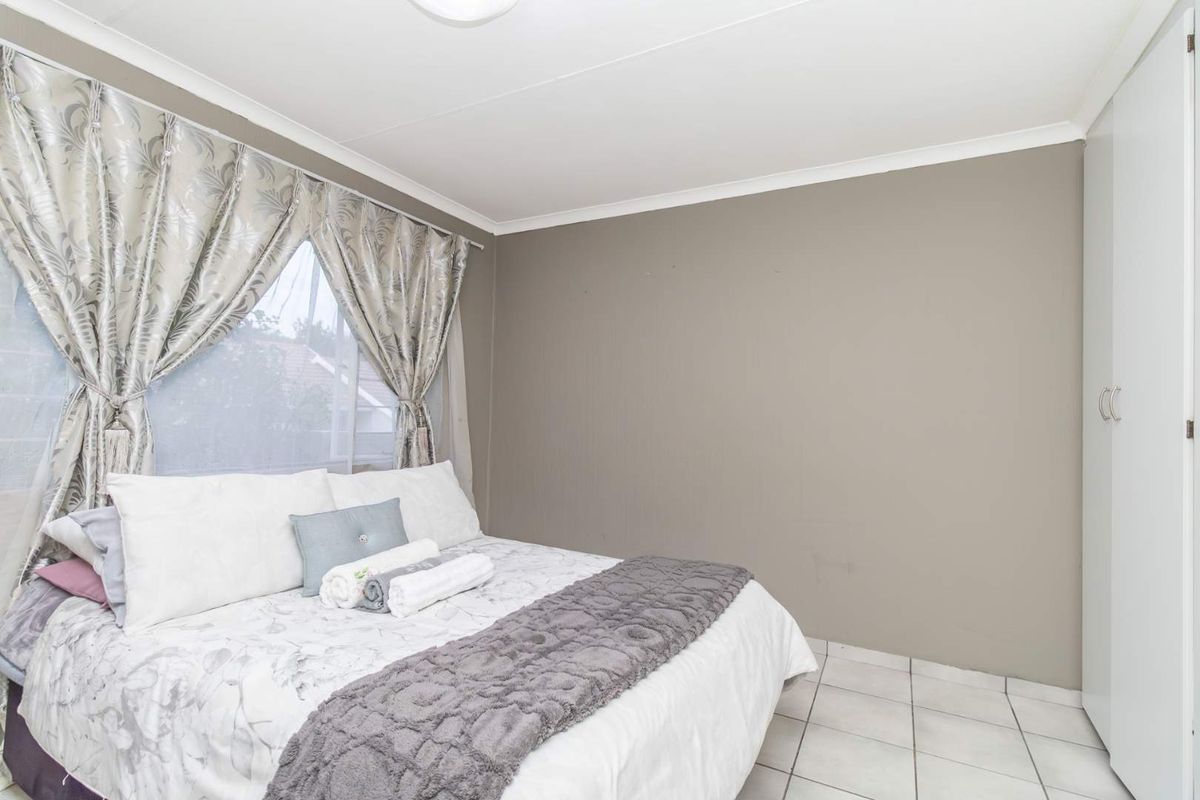 A bedroom featuring tiled flooring, built-in cupboards, and a window with curtain treatments.