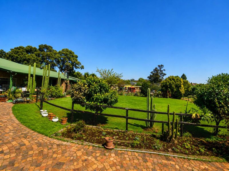 A well-maintained garden area featuring a brick paved pathway, lush green lawn, and established perimeter fencing on a small holding property.