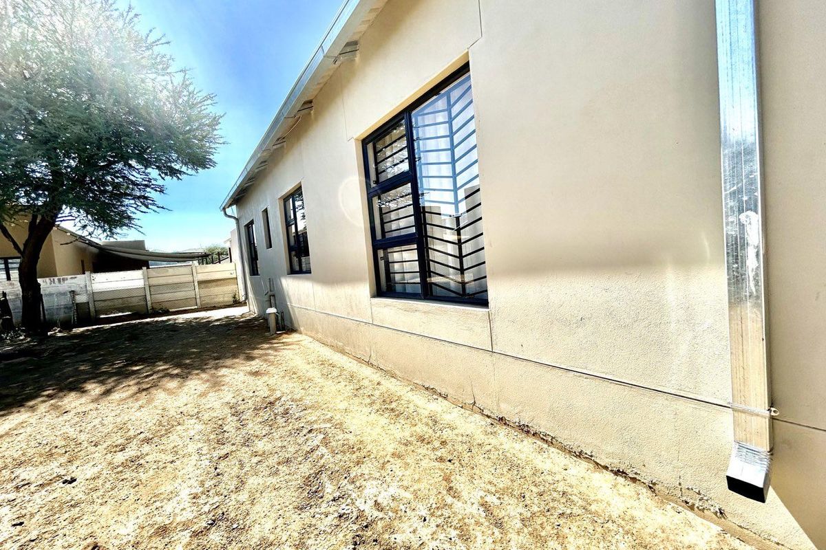 A view of the rear exterior wall of the house, featuring metal window security bars and a vertical downpipe.