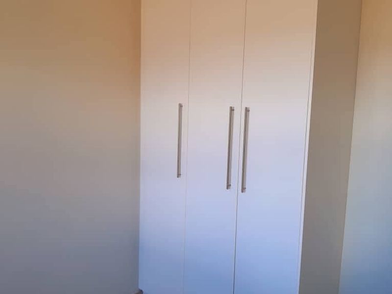 A clean, empty bedroom featuring neutral walls, tiled flooring, and a modern white built-in wardrobe with sleek handles.