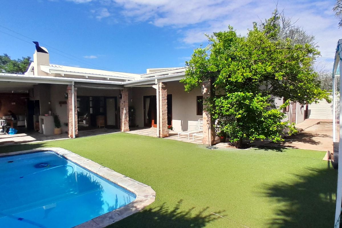 Rear exterior view featuring a swimming pool, artificial lawn, and a covered patio area with brick pillars and an outdoor fireplace.
