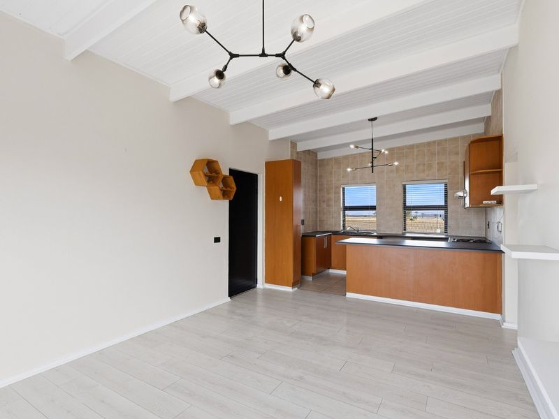 Open-plan living and kitchen area featuring exposed beam ceilings, modern light fixtures, and wood-finish cabinetry with integrated appliances.