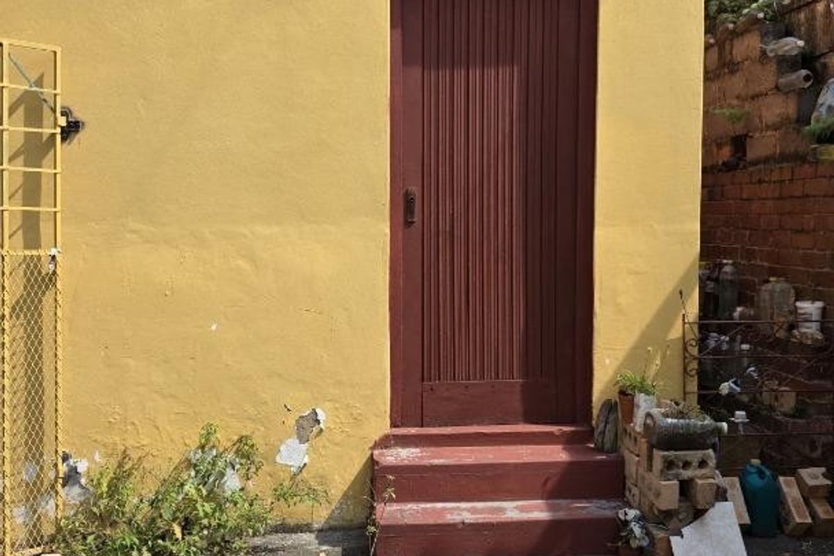Rear exterior view of the property showing a yellow facade, a single entry door with concrete steps, and asphalt paving.