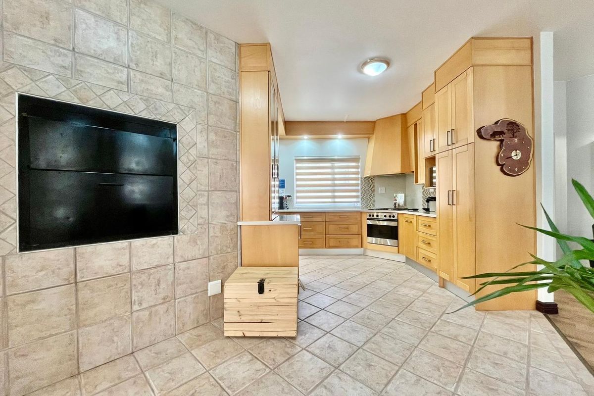 A functional kitchen featuring light wood cabinetry, tiled flooring, and a built-in indoor braai or fireplace with tiled surround.