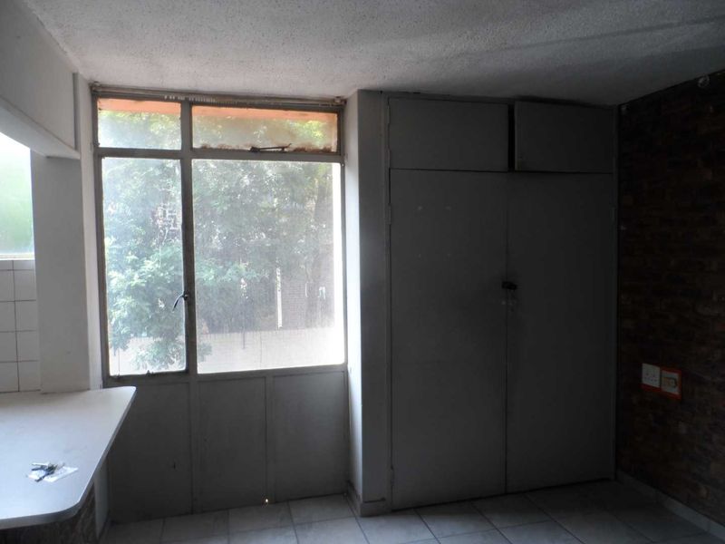 An empty bedroom featuring built-in cupboards, tiled flooring, and an exposed brick feature wall, requiring cosmetic updates to modernize the space.