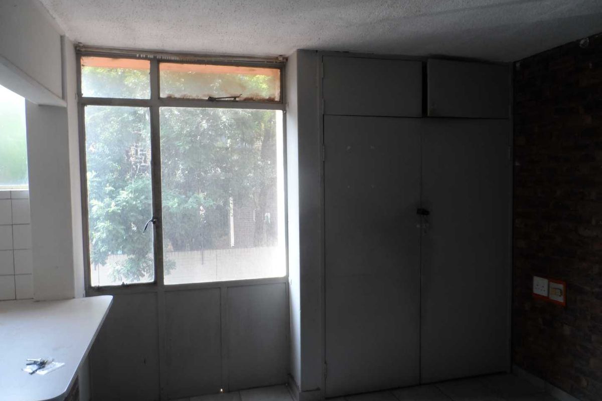 An empty bedroom featuring built-in cupboards, tiled flooring, and an exposed brick feature wall, requiring cosmetic updates to modernize the space.