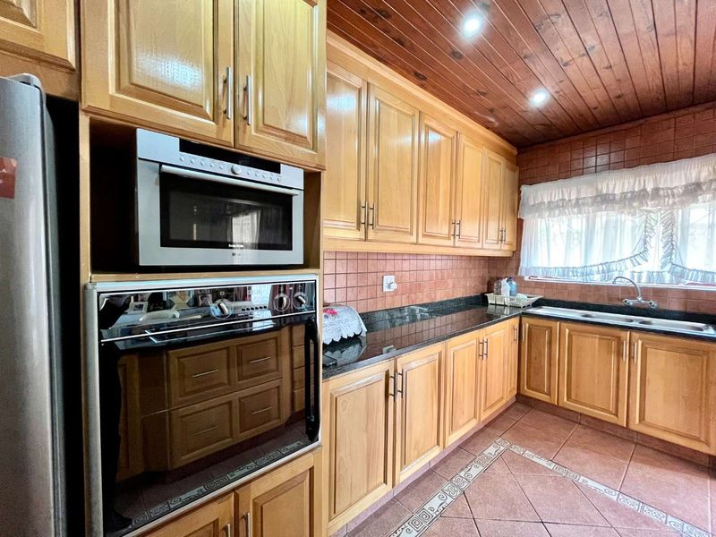 A functional kitchen featuring warm-toned wooden cabinetry, granite countertops, built-in oven and microwave, and a distinctive timber-paneled ceiling.