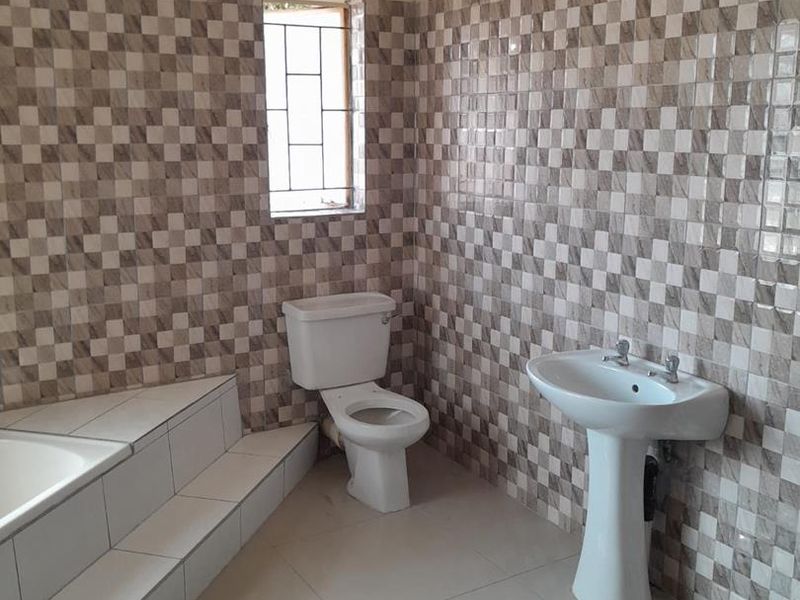 A clean, empty bathroom featuring a pedestal basin, toilet, and a tiled built-in bathtub with decorative wall tiling.