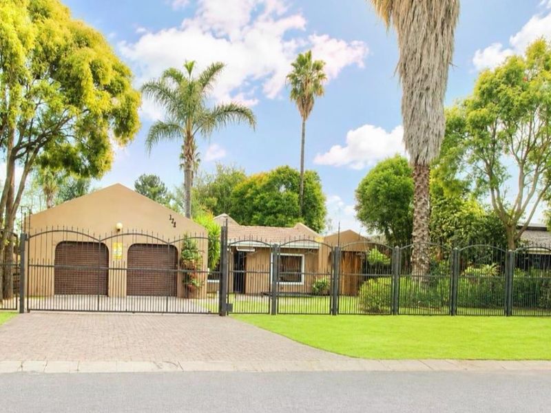 Front elevation of a residential property featuring a double garage, paved driveway, and secure wrought iron perimeter fencing set within a landscaped garden.