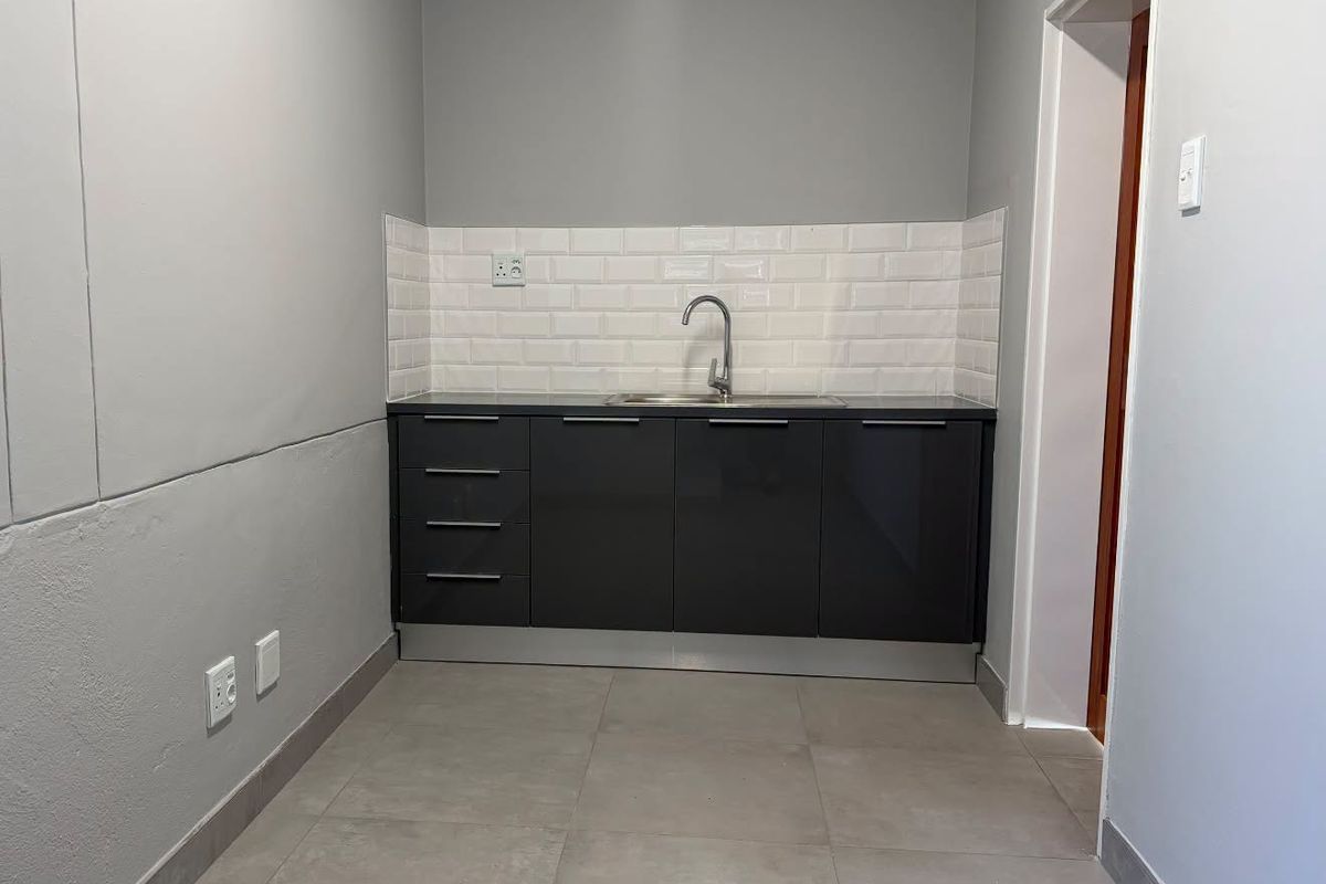 A compact, modern kitchenette featuring dark grey cabinetry, a subway tile backsplash, and a stainless steel sink, finished with neutral large format floor tiles.
