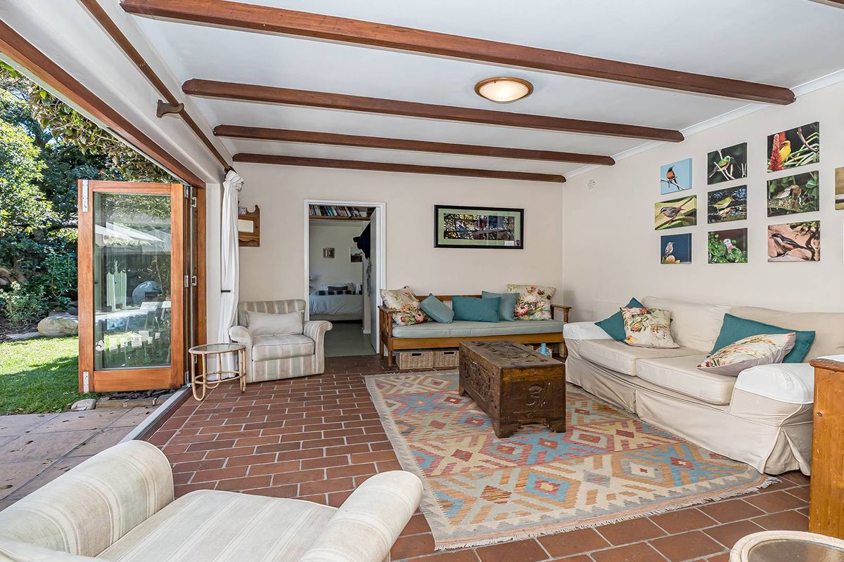 A spacious living area featuring exposed timber ceiling beams, terracotta tiled flooring, and large bi-fold doors opening directly onto a lush garden.