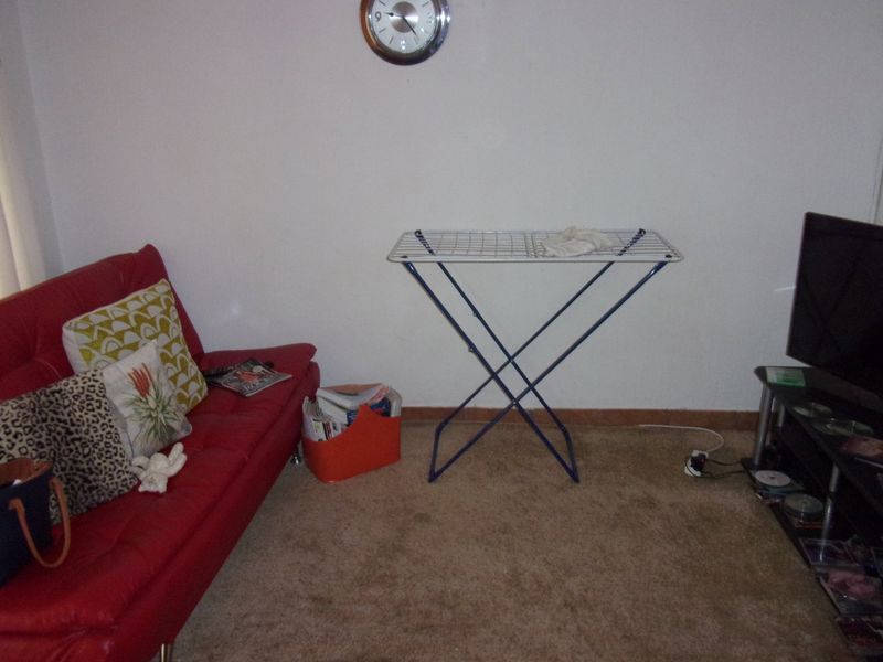 A living room area featuring carpet flooring and plain wall finishes, currently utilized as a multi-purpose space.