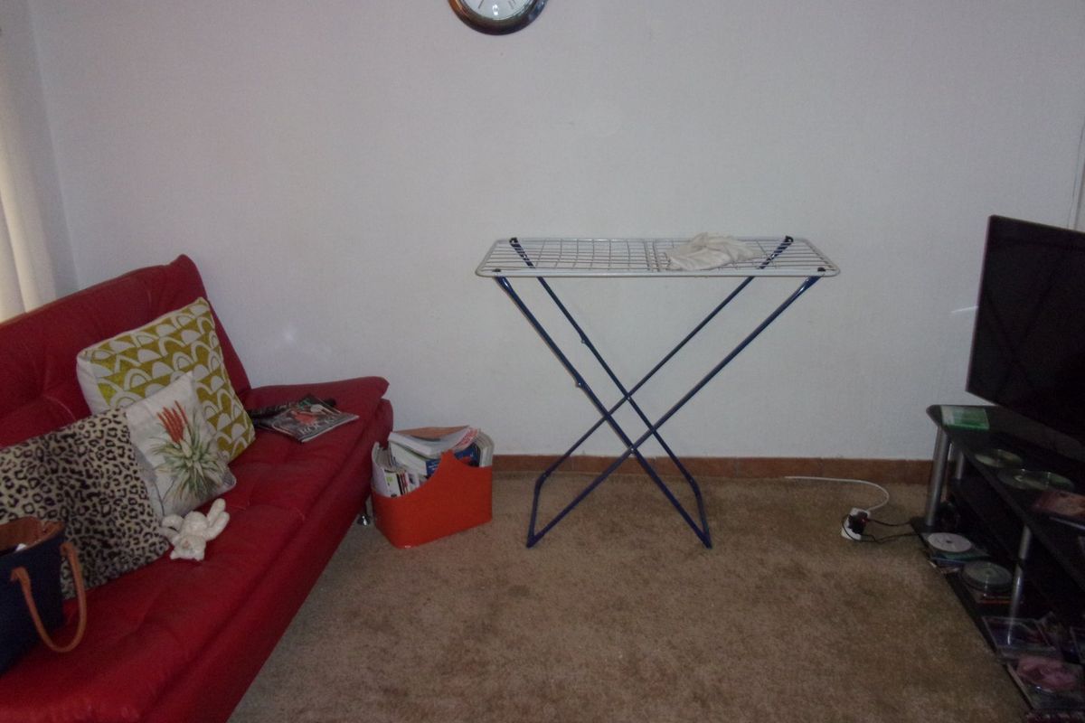 A living room area featuring carpet flooring and plain wall finishes, currently utilized as a multi-purpose space.