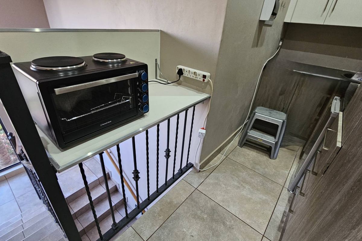 A compact kitchen area featuring tiled flooring, built-in cabinetry, and a wrought iron balustrade overlooking the staircase.