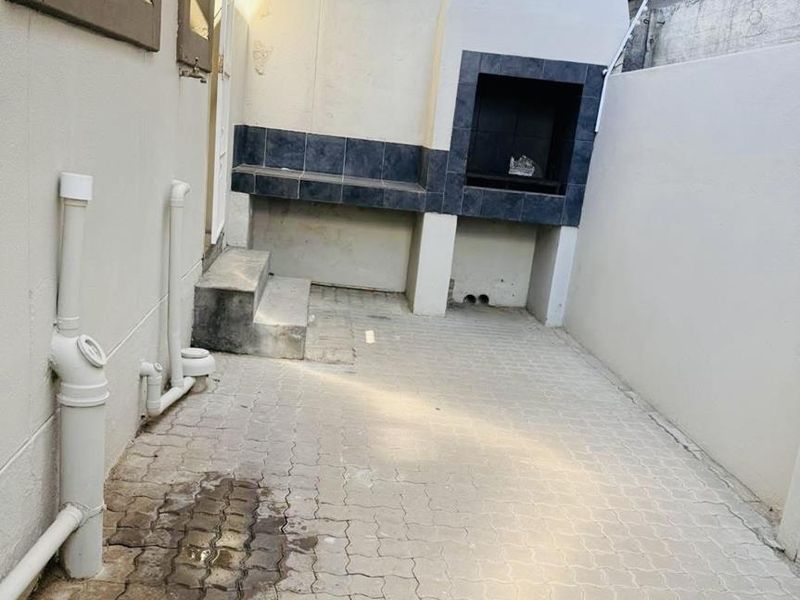 A compact outdoor patio area featuring a built-in braai with tiled counter space and paved flooring, offering a functional space for outdoor cooking.
