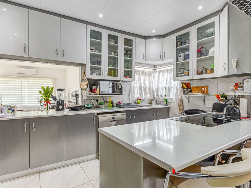 A modern, well-maintained kitchen featuring extensive built-in cabinetry, a central island with an integrated cooktop, and sleek tiled flooring.