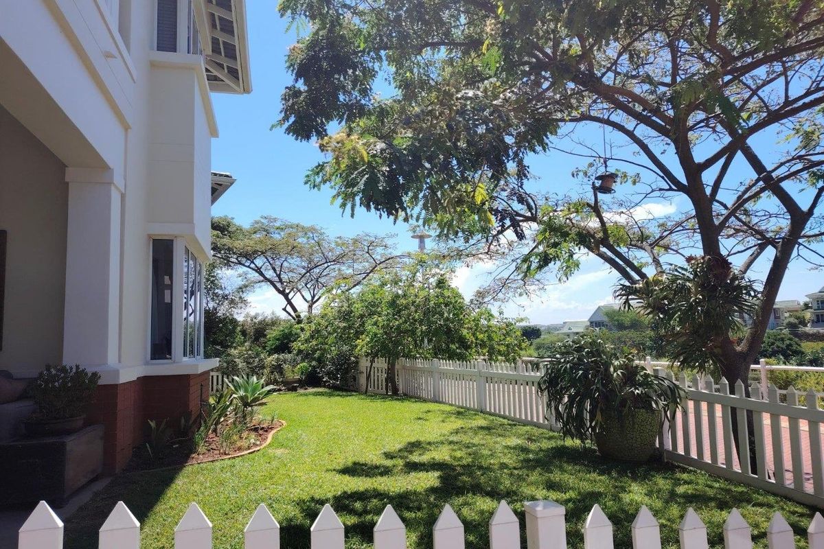 A well-maintained rear garden featuring a manicured lawn, mature trees, and a classic white picket fence bordering the property.