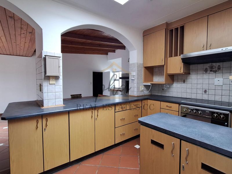 A functional kitchen featuring laminate cabinetry, built-in oven, extractor fan, and terracotta flooring, connected to an adjacent living area via a classic archway.