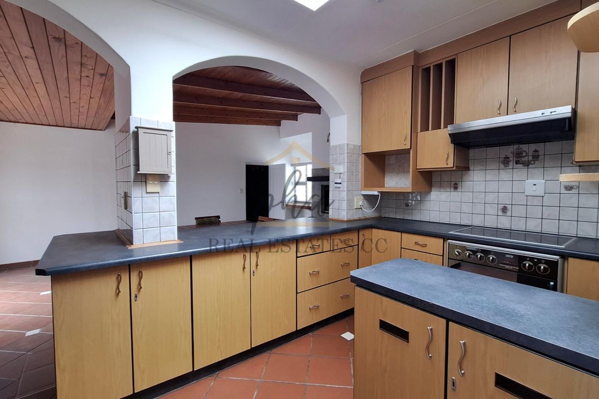 A functional kitchen featuring laminate cabinetry, built-in oven, extractor fan, and terracotta flooring, connected to an adjacent living area via a classic archway.