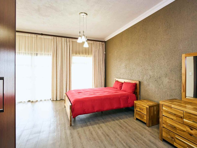 Spacious bedroom featuring laminate flooring, a textured feature wall, crown molding, and large sliding glass doors providing ample natural light.