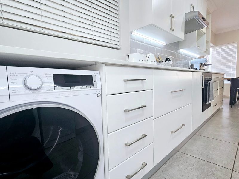 Modern kitchen featuring white cabinetry, integrated oven, extractor fan, subway tile backsplash, and an under-counter washing machine with tiled flooring.