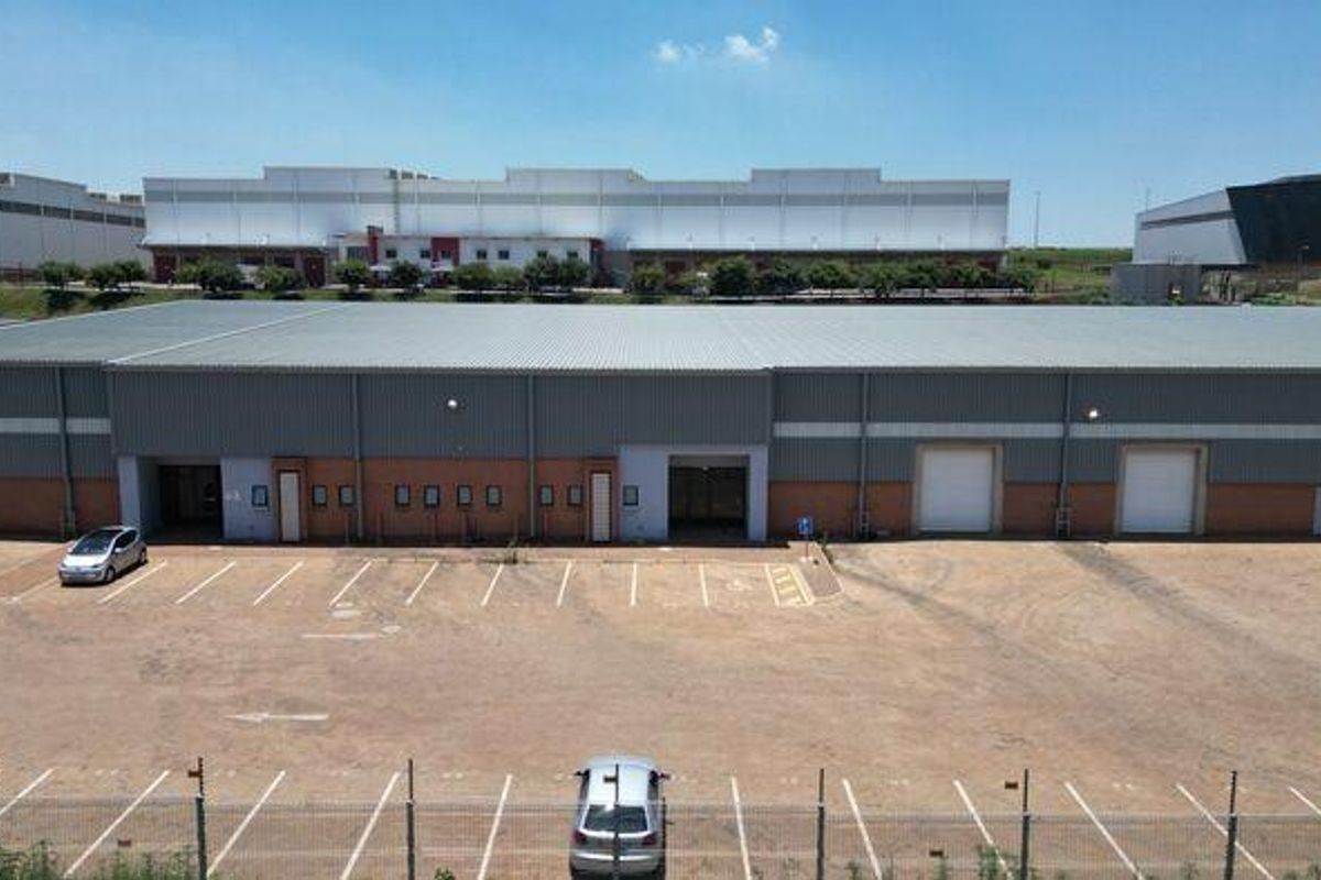 Aerial view of an industrial warehouse facility featuring multiple roller shutter doors, a large paved parking area, and secure perimeter fencing.