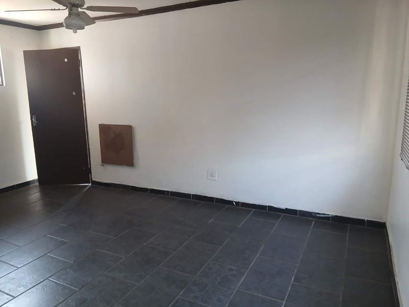 An empty living room featuring dark tiled flooring, a ceiling fan, and a neutral wall finish, ready for personalization.