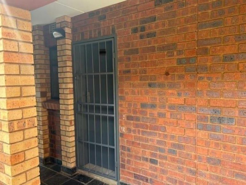 An exterior entrance area featuring a secure metal gate and traditional face-brick wall construction.