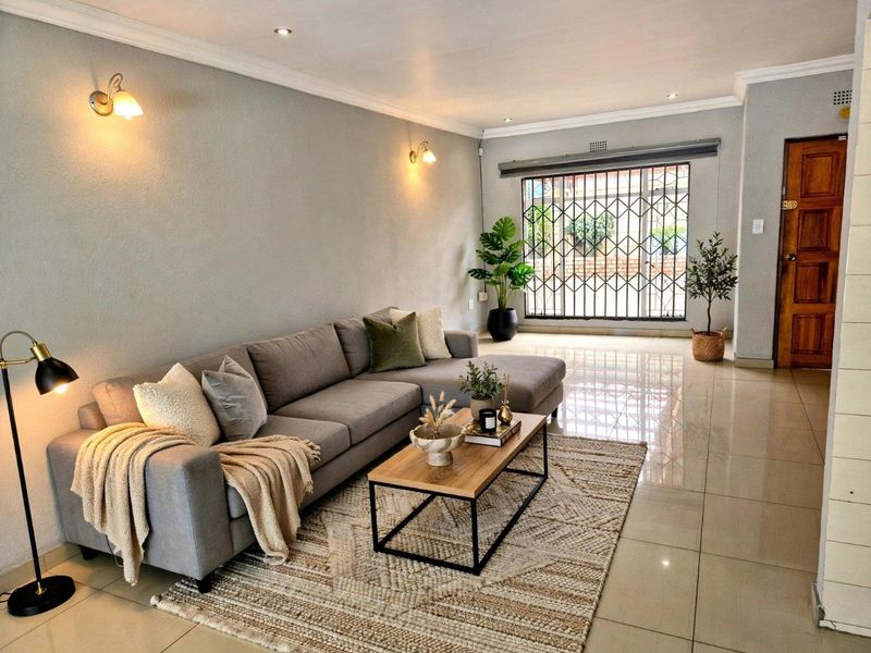 A well-maintained living room featuring neutral tiled flooring, recessed downlighting, wall sconces, and a secure entrance with a fitted security gate.