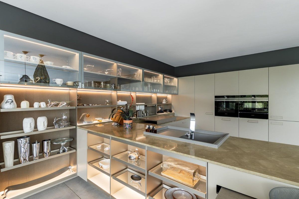 Modern kitchen featuring high-end cabinetry, integrated double ovens, stone countertops, and built-in display shelving with ambient LED lighting.
