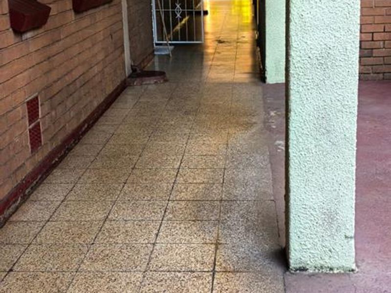 An exterior covered walkway featuring brick walls, tiled flooring, and a security gate, providing access to the apartment units.