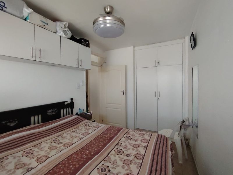 A functional bedroom featuring built-in cupboards, overhead storage units, and a ceiling fan, providing practical storage and climate control solutions.