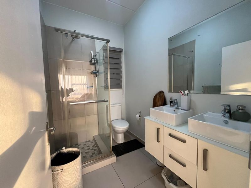 Modern bathroom featuring a double vanity with dual basins, a glass-enclosed shower, and neutral floor tiling.