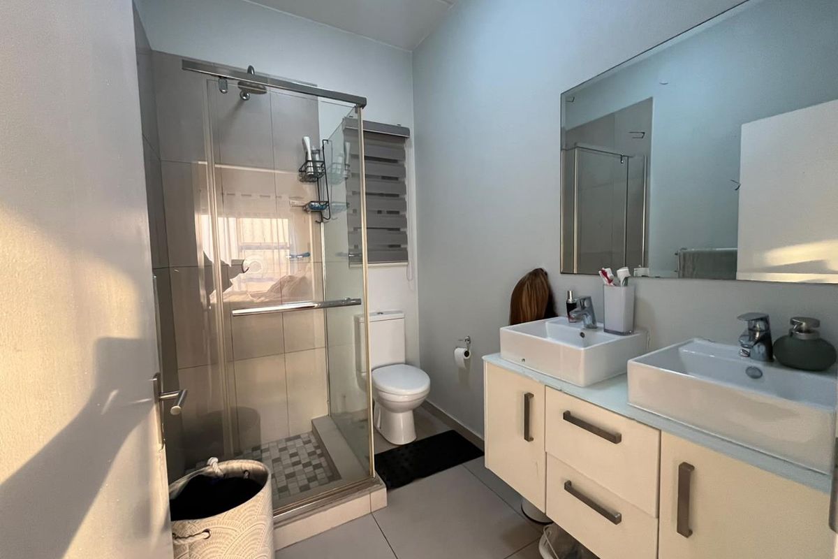 Modern bathroom featuring a double vanity with dual basins, a glass-enclosed shower, and neutral floor tiling.