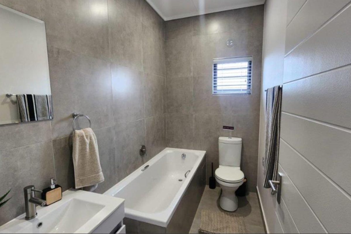 Modern bathroom featuring large-format grey wall tiles, a built-in bathtub, a sleek vanity with basin, and a toilet.
