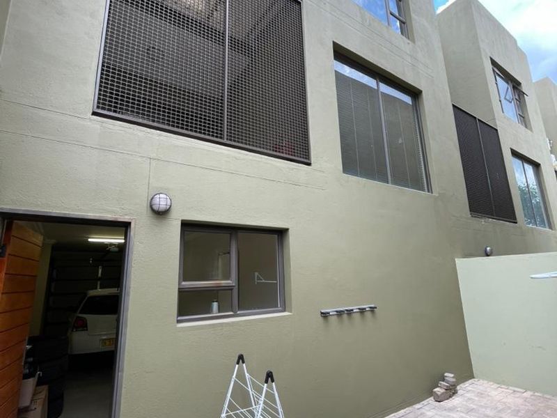 Rear exterior view of the townhouse featuring a paved courtyard, security mesh window screens, and direct access to the garage.