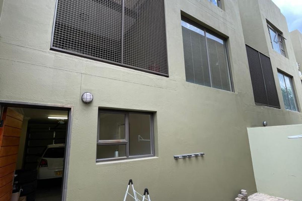 Rear exterior view of the townhouse featuring a paved courtyard, security mesh window screens, and direct access to the garage.