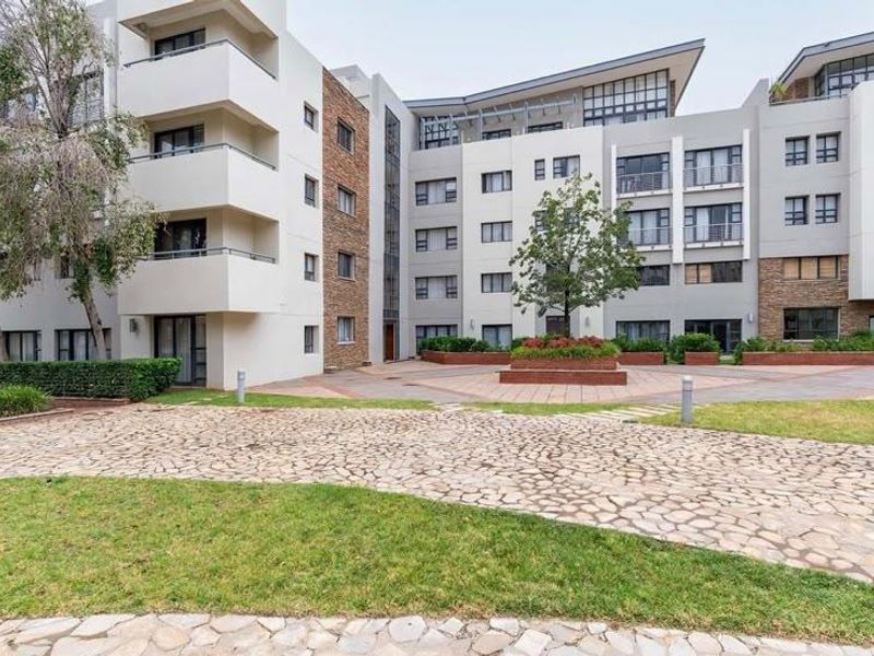 A view of the apartment complex rear courtyard featuring stone paving, landscaped garden beds, and multiple levels of private balconies.
