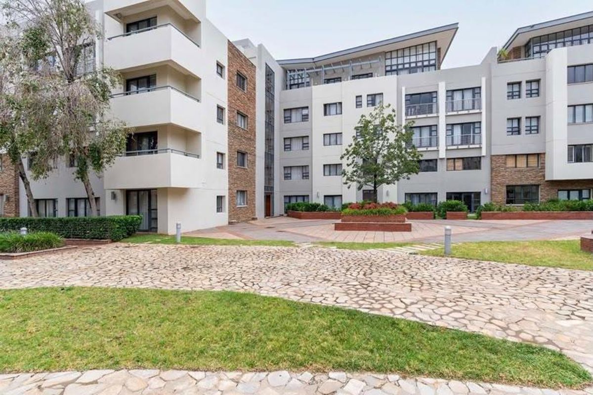 A view of the apartment complex rear courtyard featuring stone paving, landscaped garden beds, and multiple levels of private balconies.
