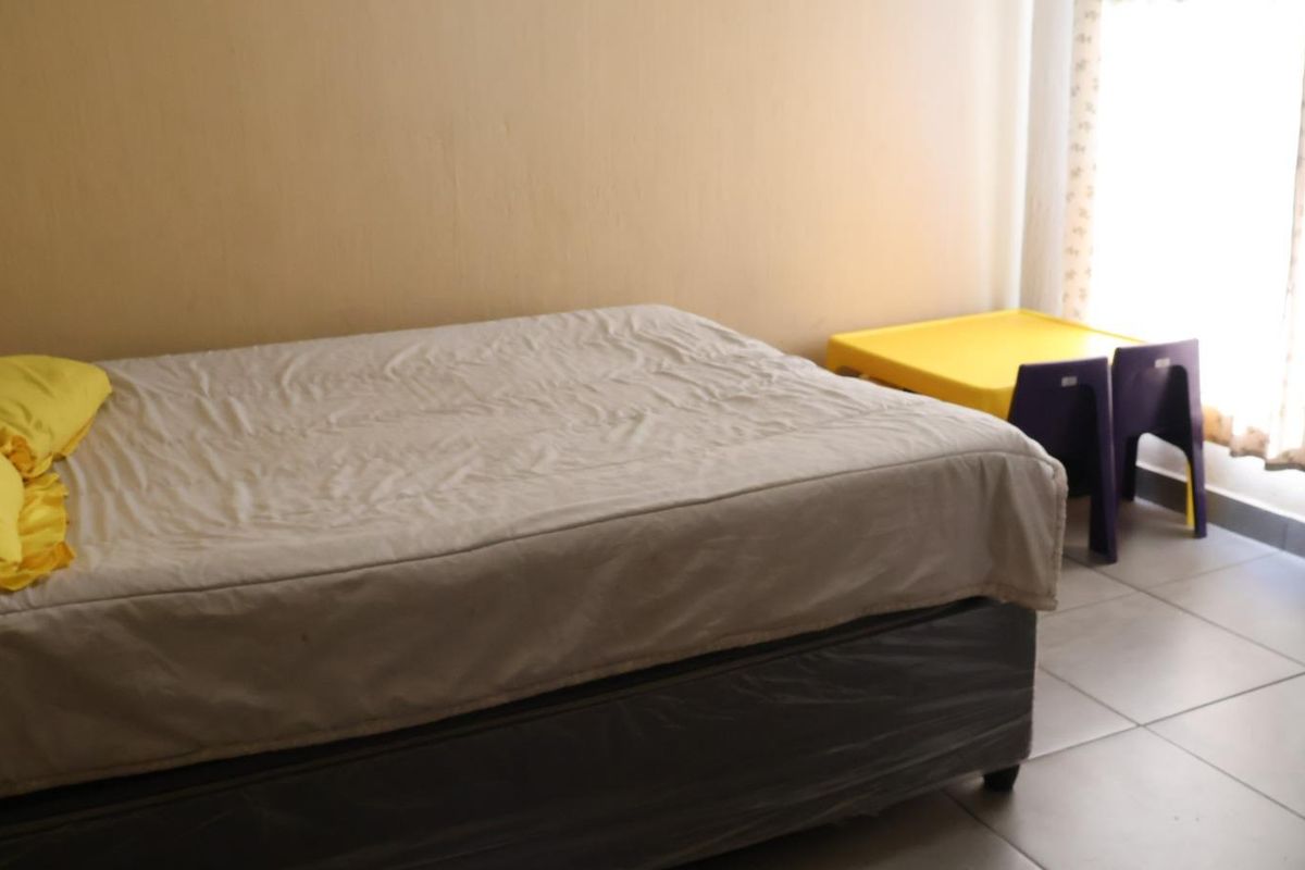 A simple bedroom featuring tiled flooring and natural light from the window.