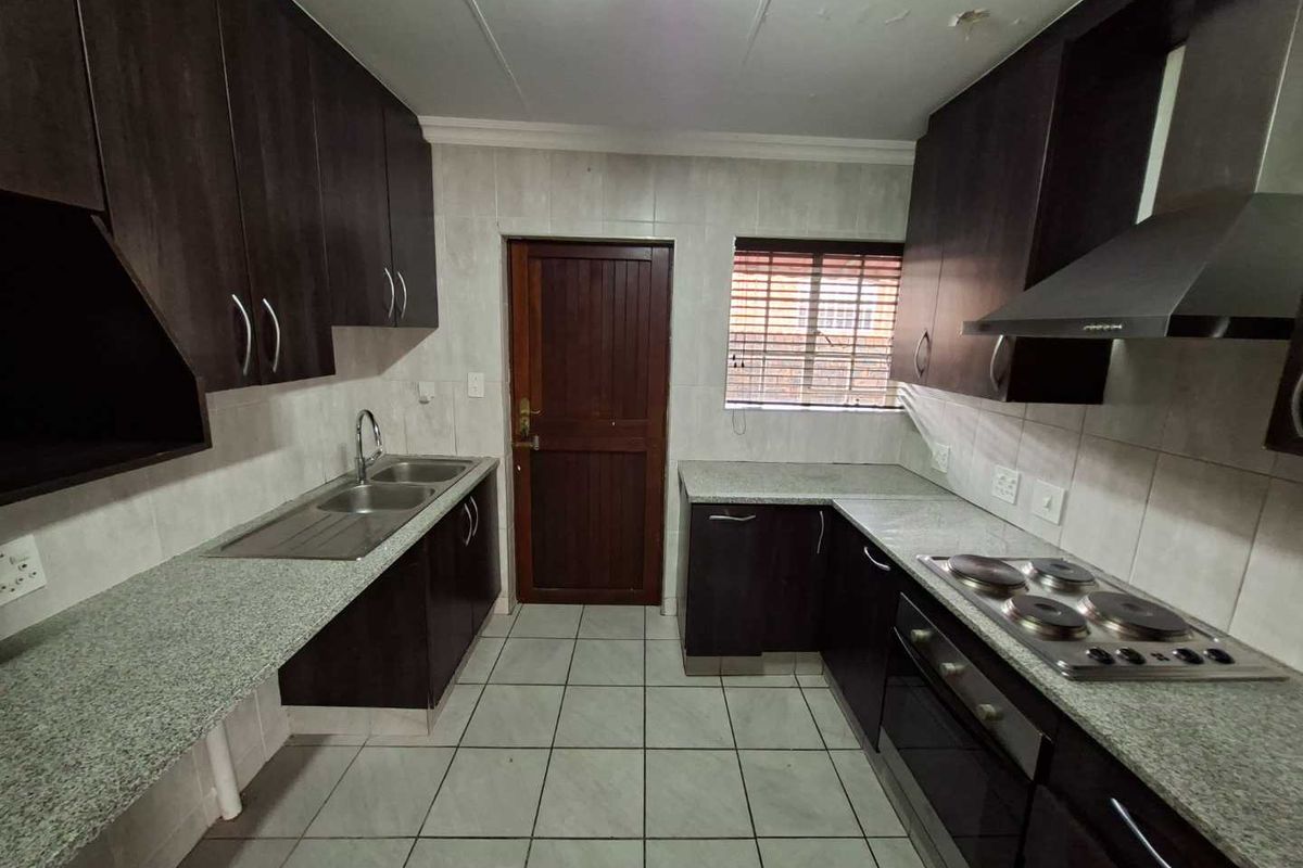 Functional kitchen featuring dark wood cabinetry, granite countertops, built-in oven and hob, and tiled flooring with direct exterior access.