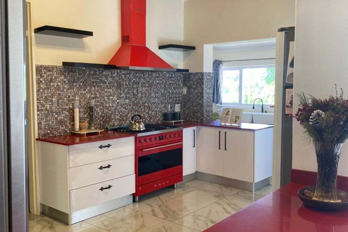 Modern kitchen featuring a striking red Smeg range cooker, matching extractor hood, red countertops, mosaic tile backsplash, and vaulted timber-paneled ceilings.