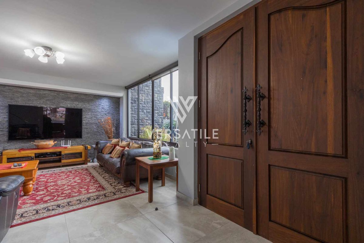 Living room featuring large double wooden entrance doors, tiled flooring, and a textured stone feature wall.