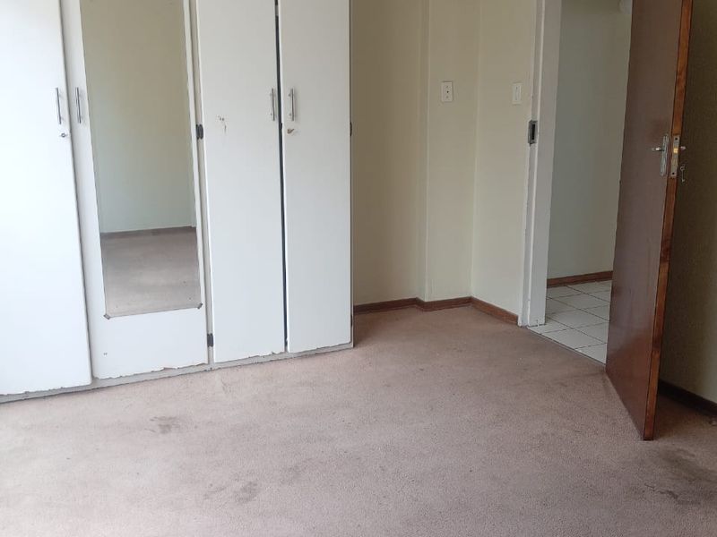 A vacant bedroom featuring built-in cupboards with a mirrored panel and neutral wall finishes, requiring new flooring to refresh the space.