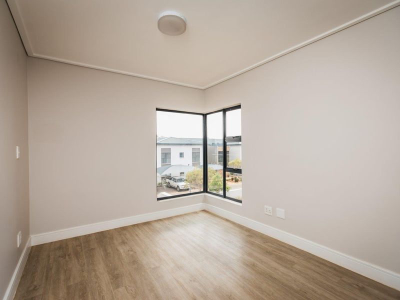 A bright, empty bedroom featuring modern laminate flooring, neutral walls, and a corner window providing natural light.