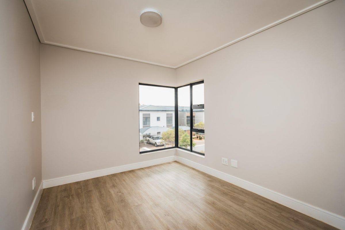 A bright, empty bedroom featuring modern laminate flooring, neutral walls, and a corner window providing natural light.