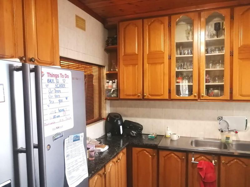 A functional kitchen featuring traditional timber cabinetry, glass-fronted display units, a stainless steel sink, and a timber-paneled ceiling.