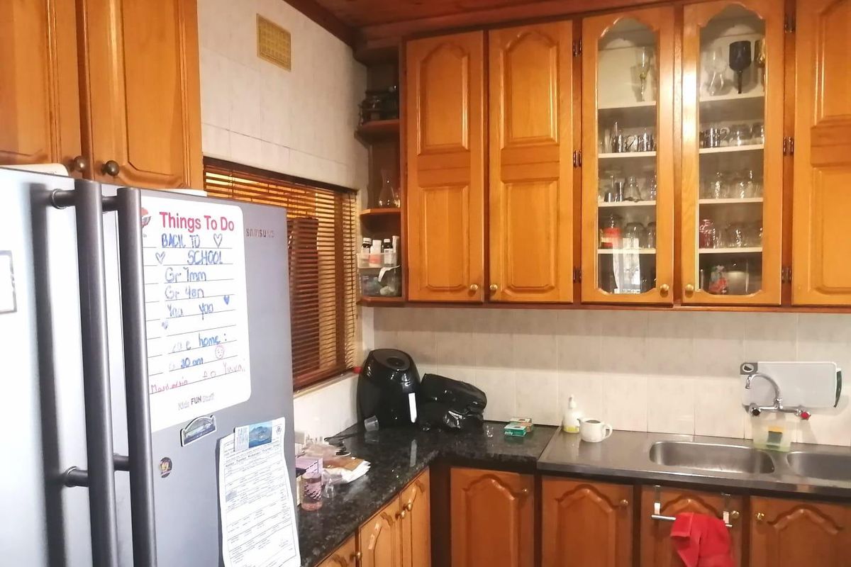 A functional kitchen featuring traditional timber cabinetry, glass-fronted display units, a stainless steel sink, and a timber-paneled ceiling.