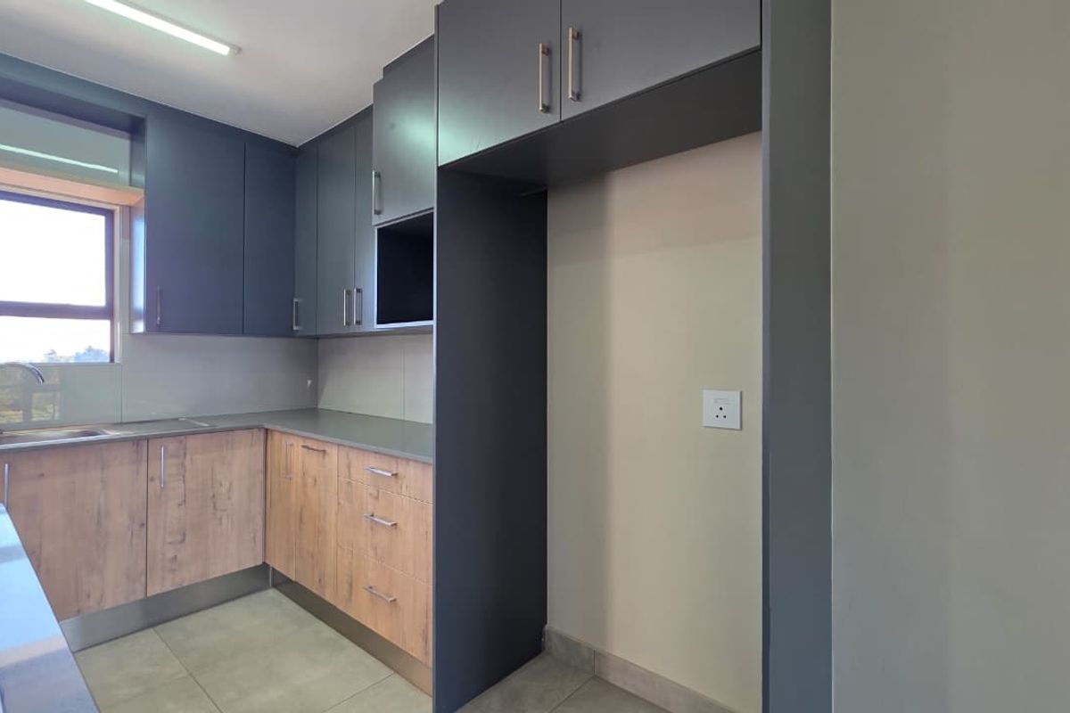 Modern kitchen featuring two-tone cabinetry, laminate countertops, integrated hob, and a dedicated refrigerator alcove with tiled flooring.