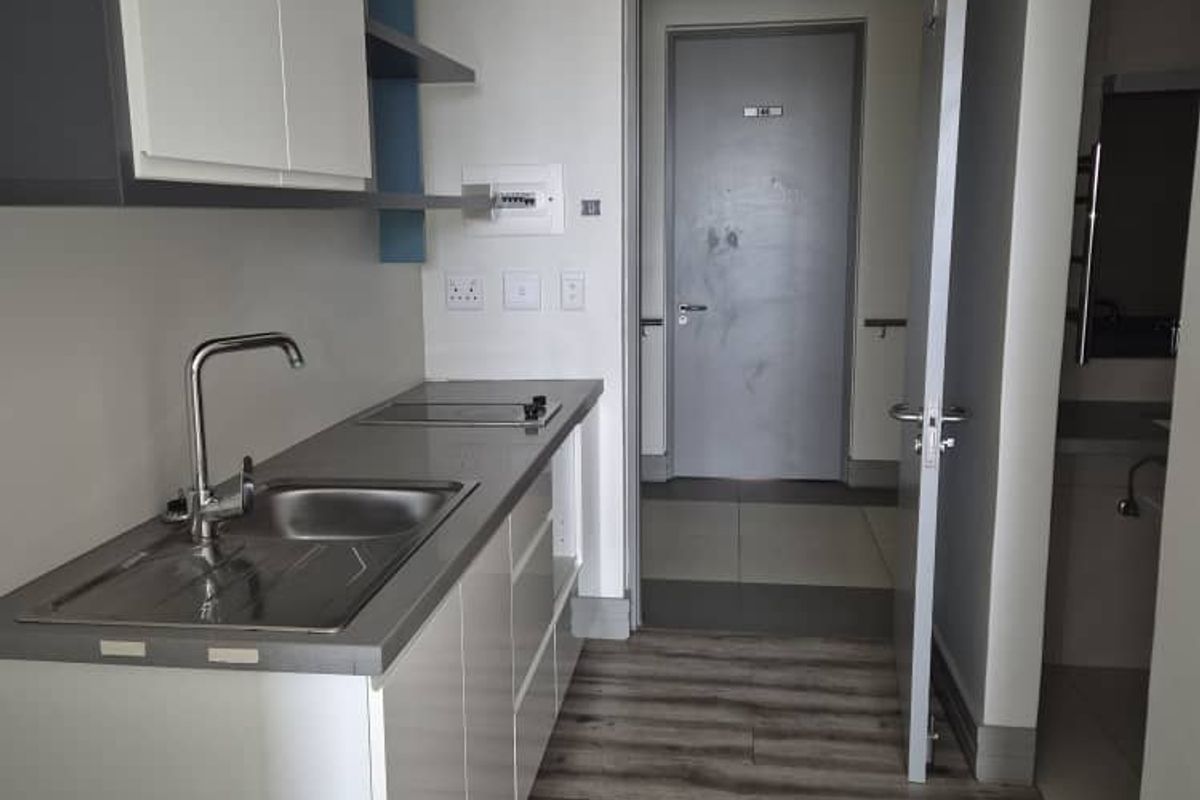 Compact kitchenette featuring modern cabinetry, integrated sink, and sleek countertop, leading into a hallway with tiled flooring and access to a separate room.